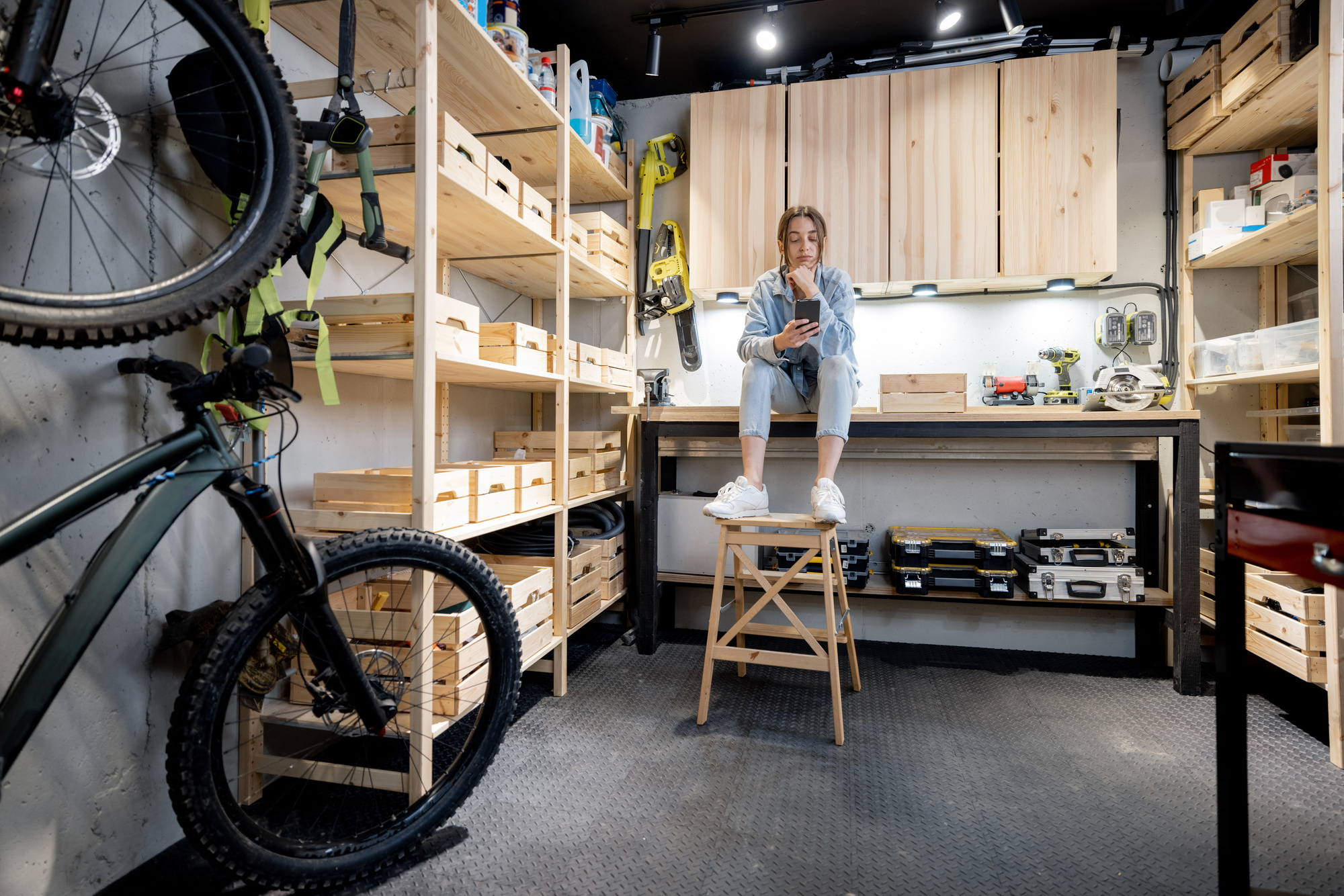 Well equipped home workshop with bicycles, wooden shelves and woman sitting on a workbench